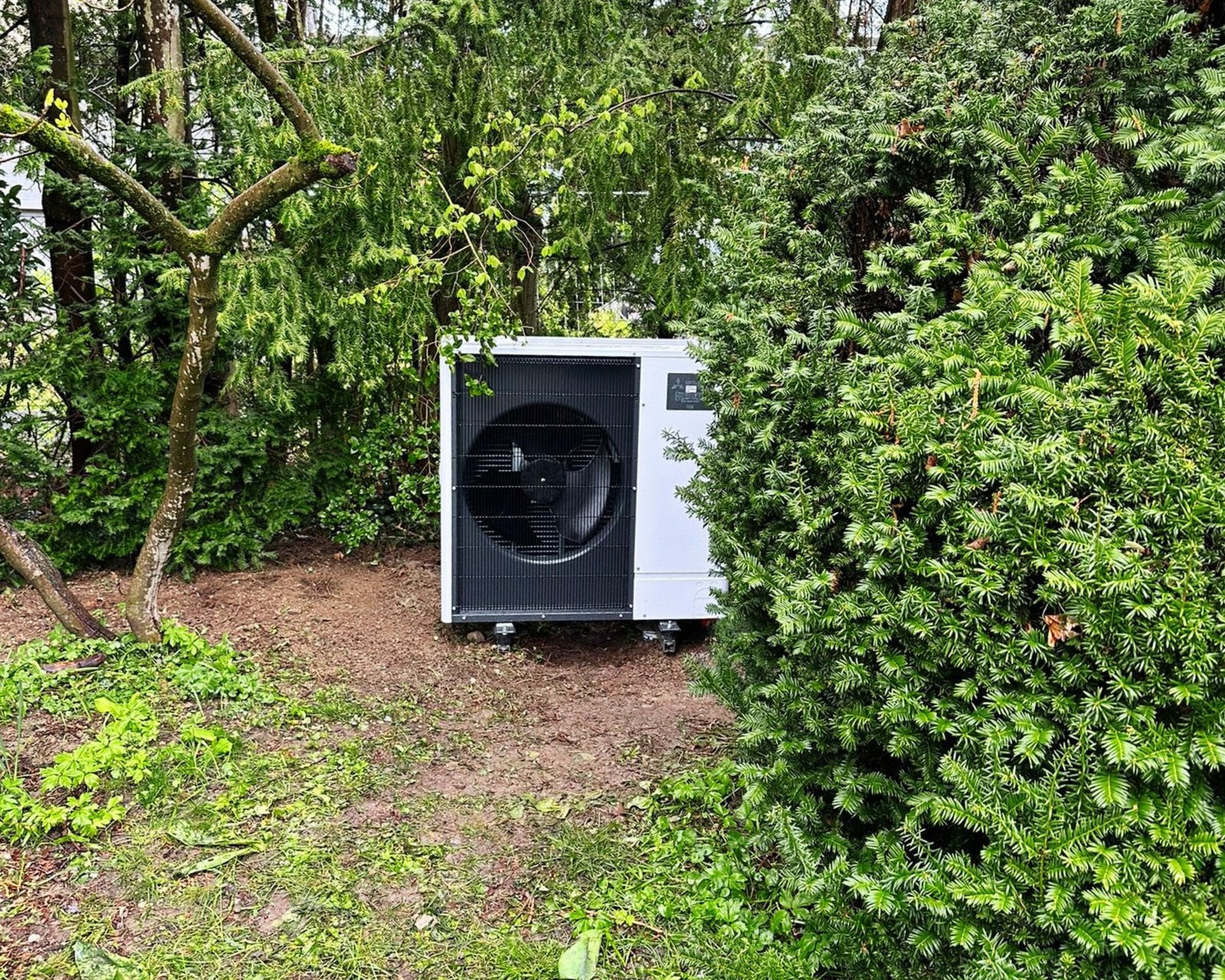 Image d'une PAC dans un buisson, il s'agit de la pompe à chaleur Mitsubishi de chez AFM